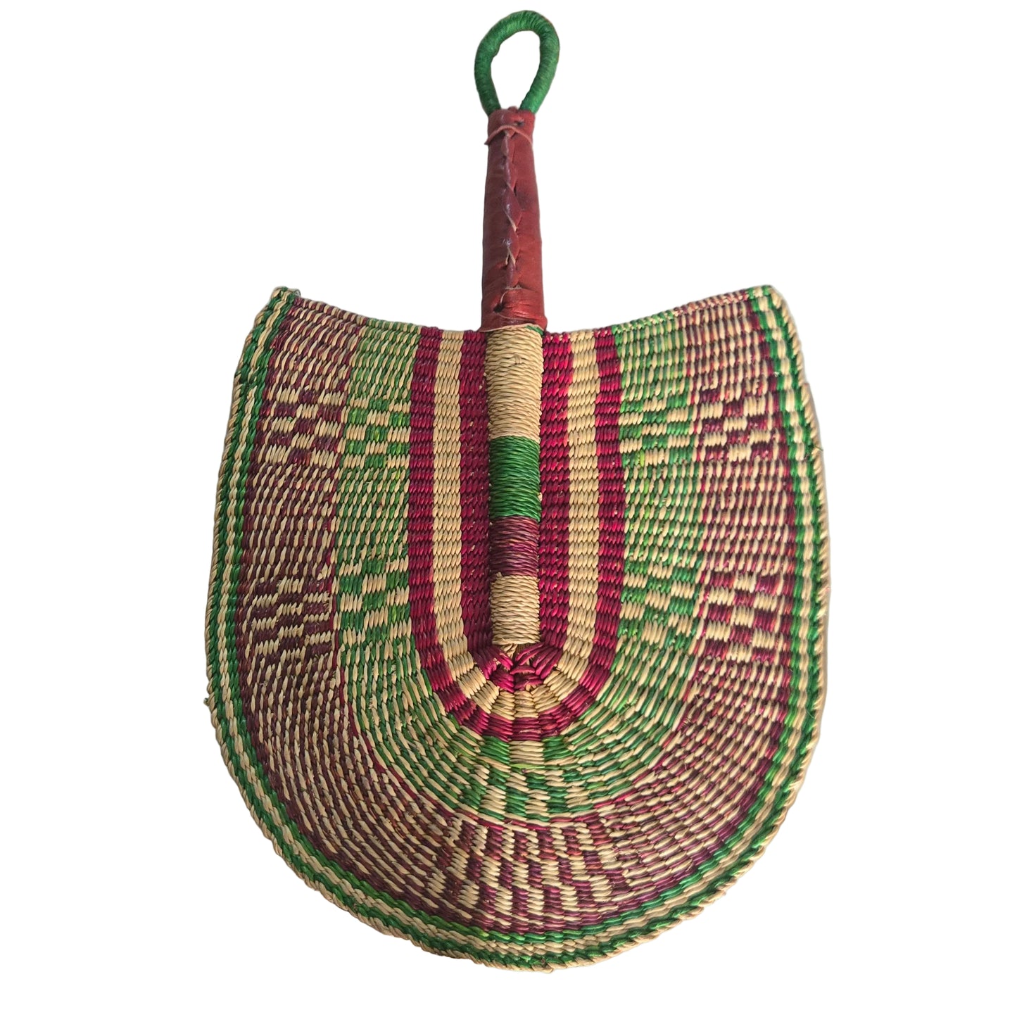 A hand-woven semicircular fan or shield-shaped accessory with a wrapped handle, placed on a white plastic tray. The woven body features concentric bands of green, red, beige, and brown in geometric patterns, with a green loop handle.