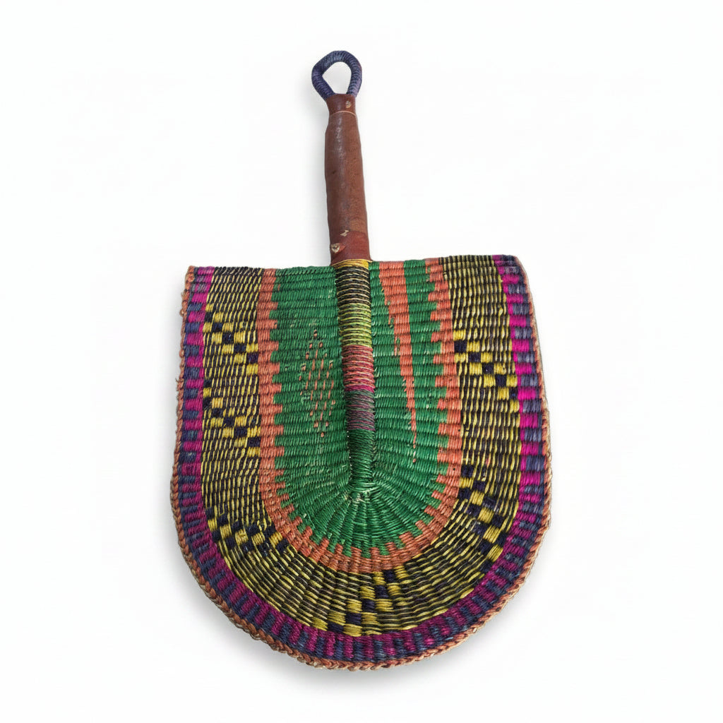 A hand-woven semicircular fan with a wooden handle, featuring intricate geometric patterns in green, pink, orange, yellow, and purple, displayed on a white plastic tray.