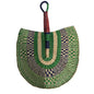 A hand-woven palm fan with a green, beige, and navy pattern, resting on a white plastic tray in an indoor setting.