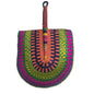 A hand-woven semicircular fan with a wooden handle, featuring vibrant concentric patterns of green, yellow, orange, purple, and pink, resting on a white plastic tub.