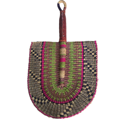 A hand-woven palm fan with a brown leather handle and a multicolored woven blade, resting on a white plastic tub in an indoor setting.