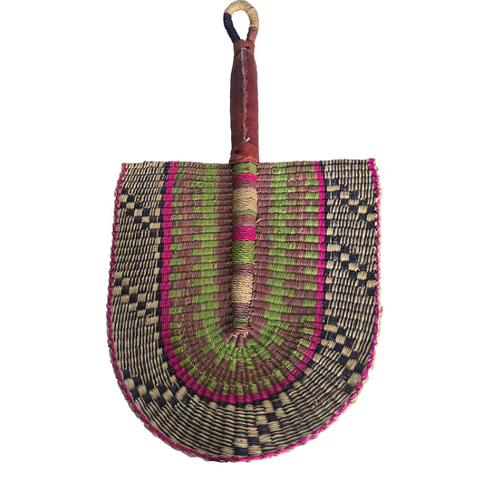A hand-woven palm fan with a brown leather handle and a multicolored woven blade, resting on a white plastic tub in an indoor setting.
