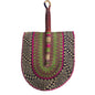 A hand-woven palm fan with a brown leather handle and a multicolored woven blade, resting on a white plastic tub in an indoor setting.