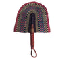 A hand-woven traditional fan with a curved head featuring concentric patterns of red, blue, black, and beige, and a brown leather handle, resting on a white plastic tub.