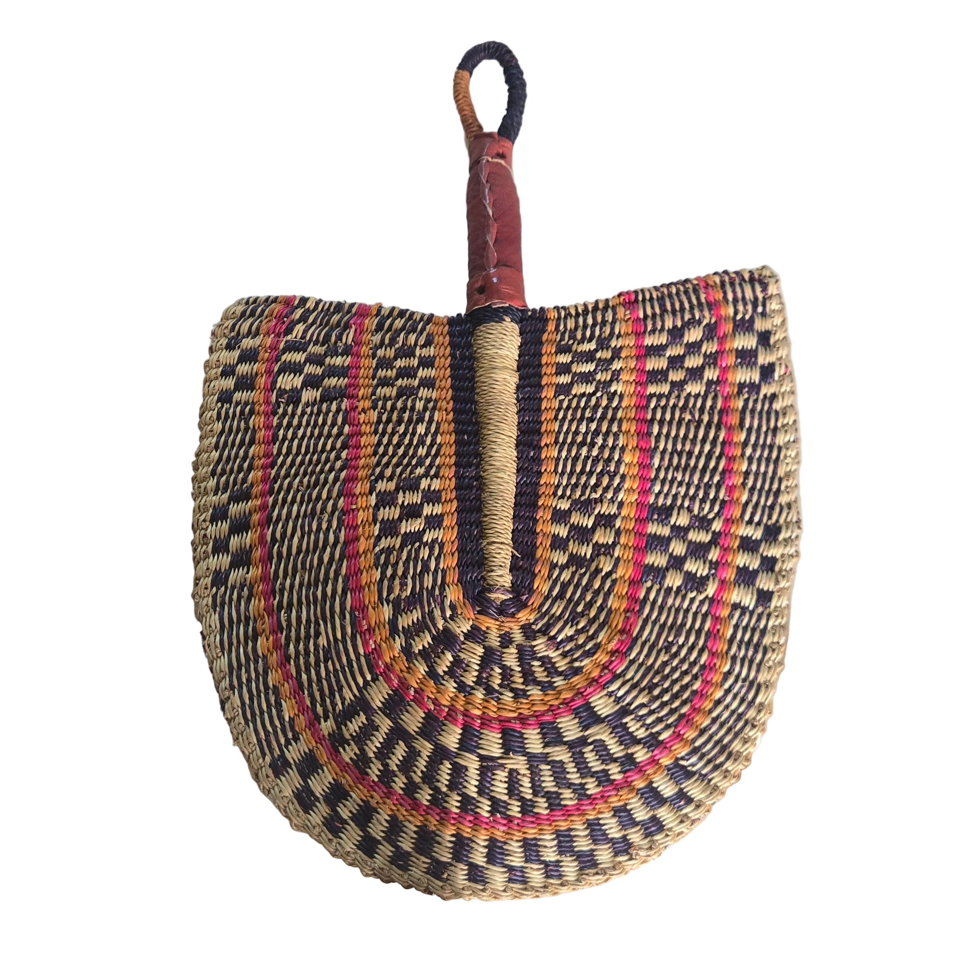 A hand-woven straw fan with a brown leather handle, featuring concentric patterns of black, red, orange, and beige, resting on a white plastic tub in an indoor setting.