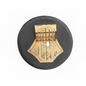 A hand holds a handmade circular kalimba thumb piano made from a dark gray or black round disc with a light wood belly and metal tuning keys. The keys have small red, blue, and white beads.