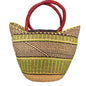 A woven straw tote bag with dark brown and lime green geometric stripes and thick red handles. 