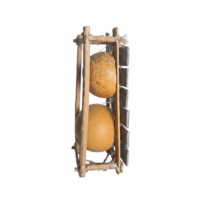 A handmade double gourd harp or wind instrument made from two natural gourds in a bamboo frame, standing on a metal tray with a DHL box in the background.